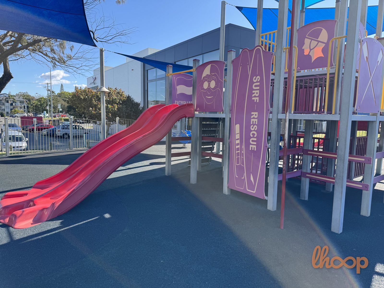 Close view of the red double slide and the surf rescue board panel on the climbing tower.